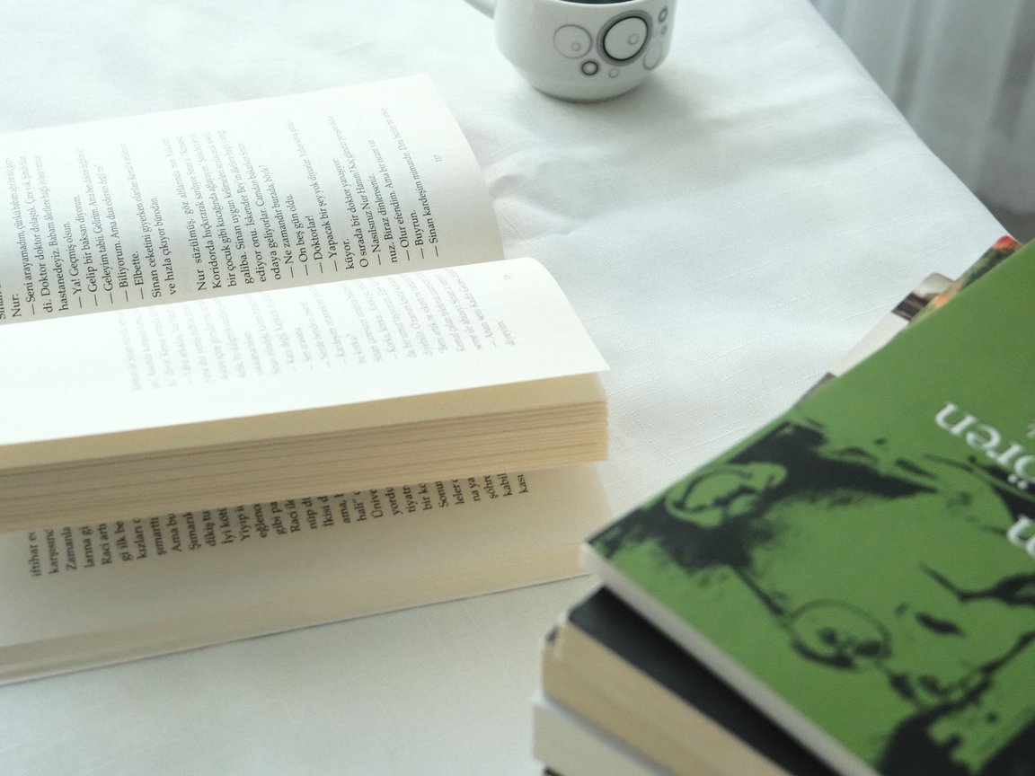 Books and a cup of coffee on a white table by a window.