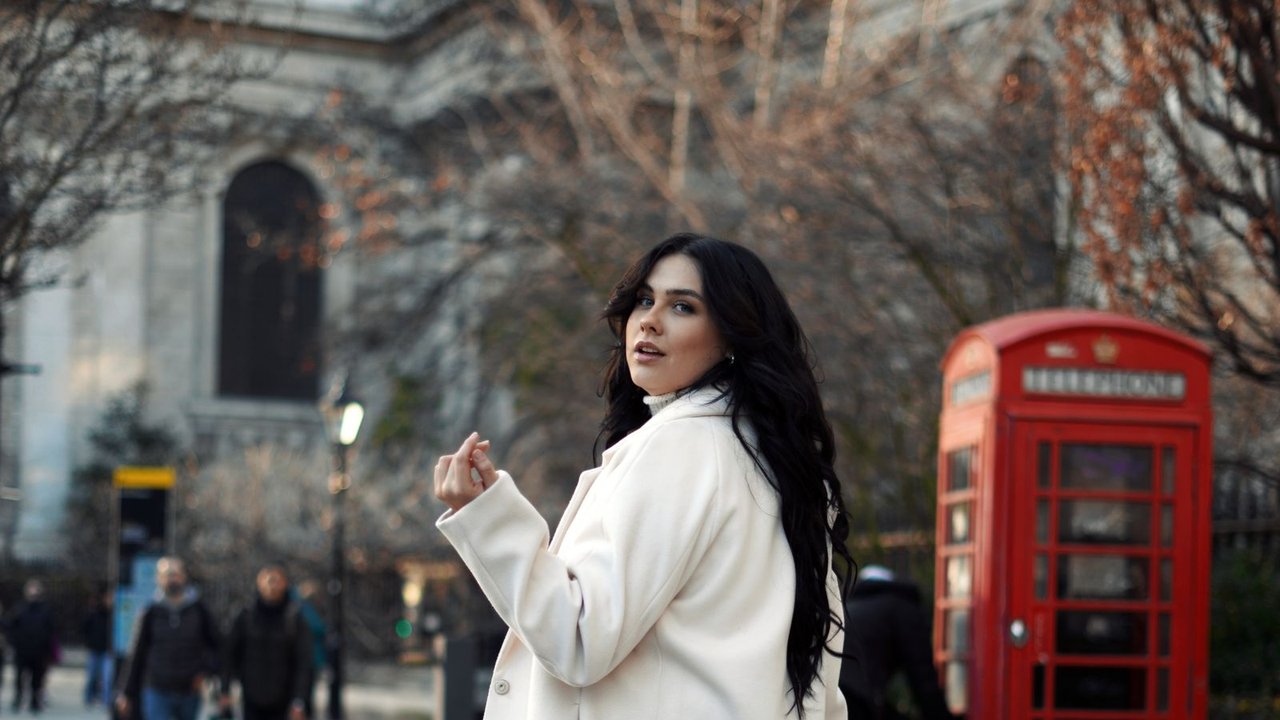 A woman in a white coat on a London street beside a red phone box.